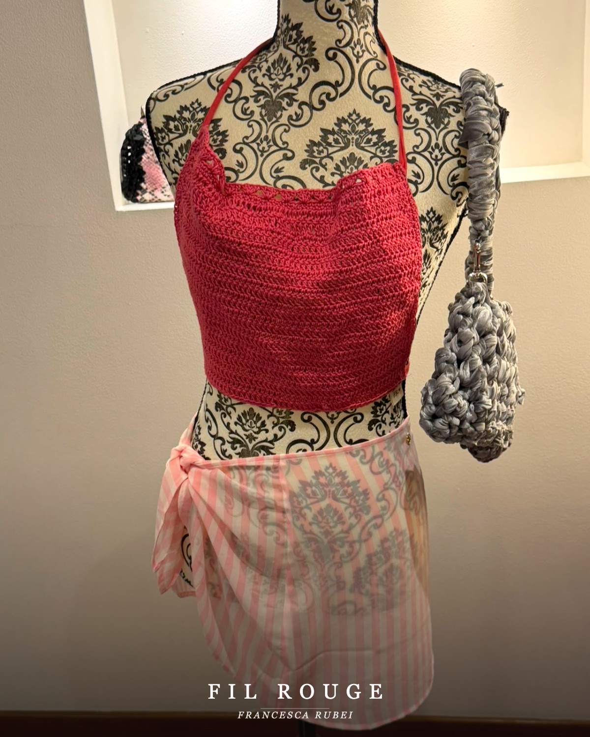 Hand-crocheted red halter top styled with a pink sarong and grey crochet bag on a vintage mannequin